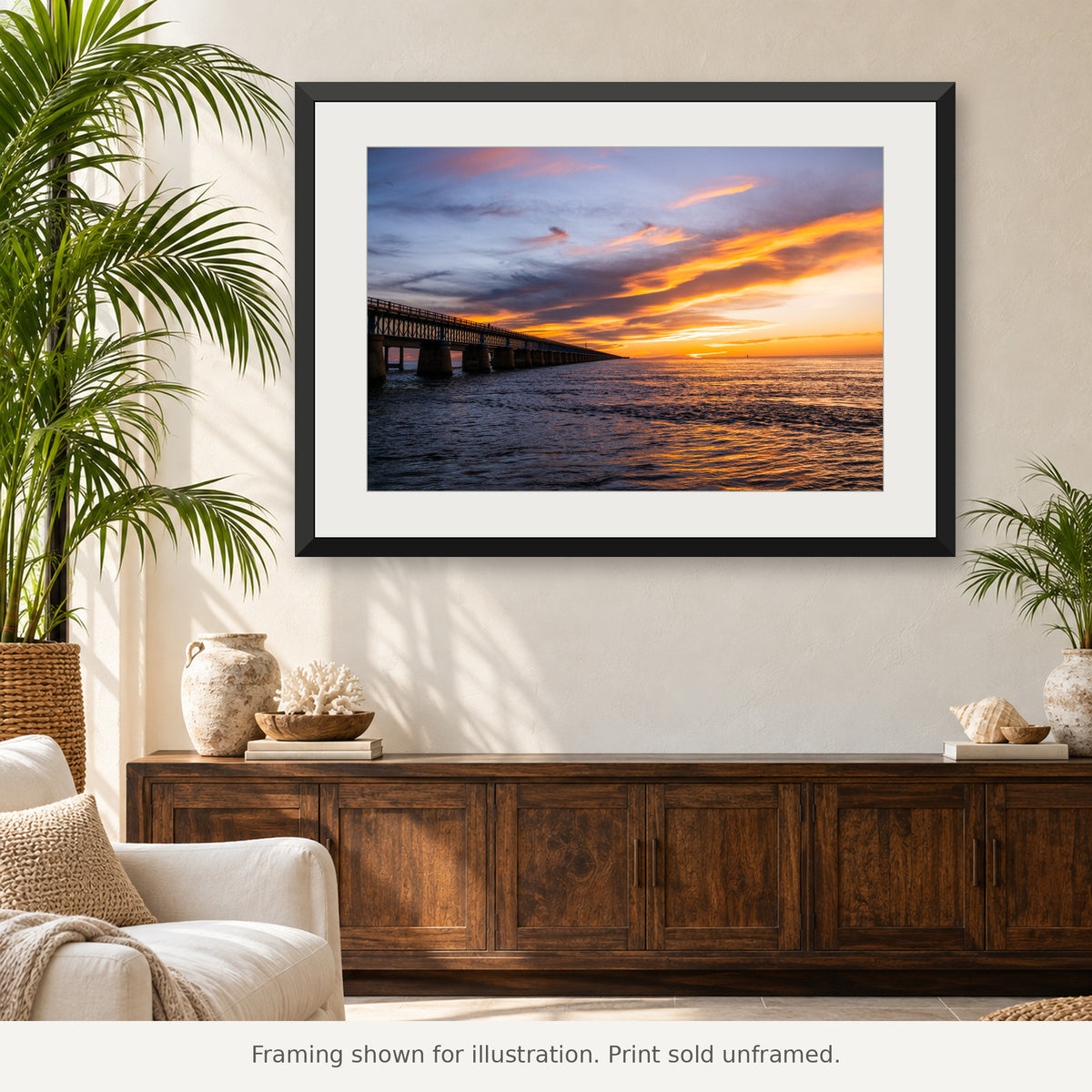 Seven Mile Bridge at dusk displayed above a dark wood console in a neutral living room with tropical palms. Print sold unframed.