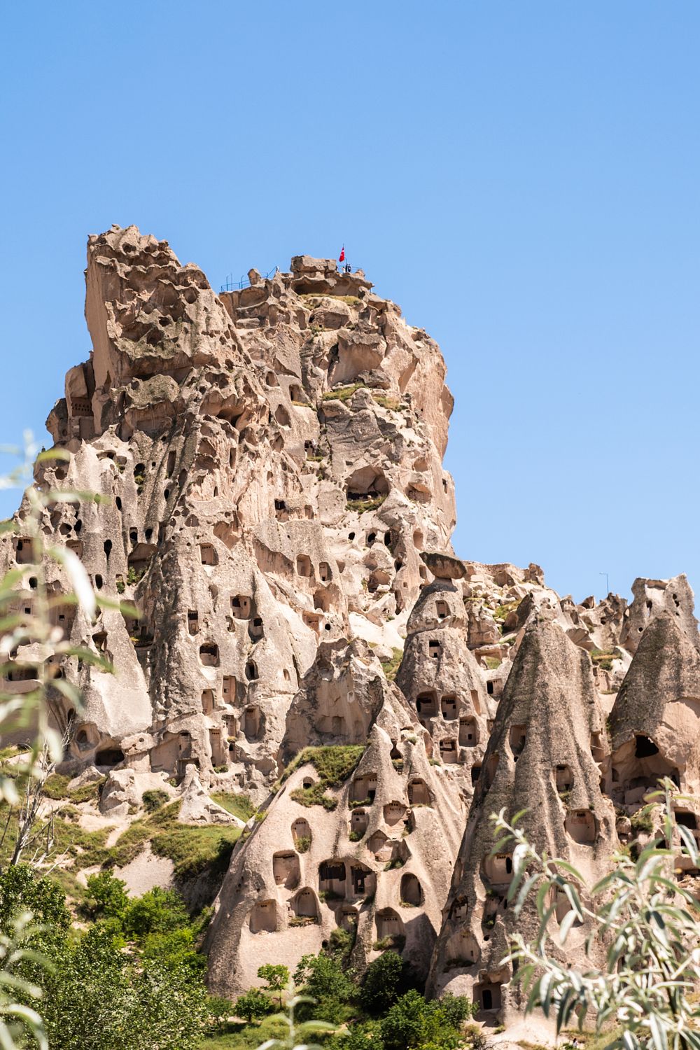 Rock dwellings carved into pale stone cliffs in Uçhisar, Cappadocia, Turkey, beneath a clear blue sky.