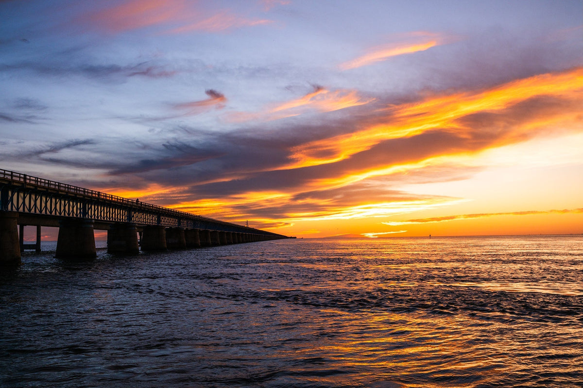 Seven Mile Bridge at dusk beneath a dramatic orange and blue sunset sky over the water in the Florida Keys.