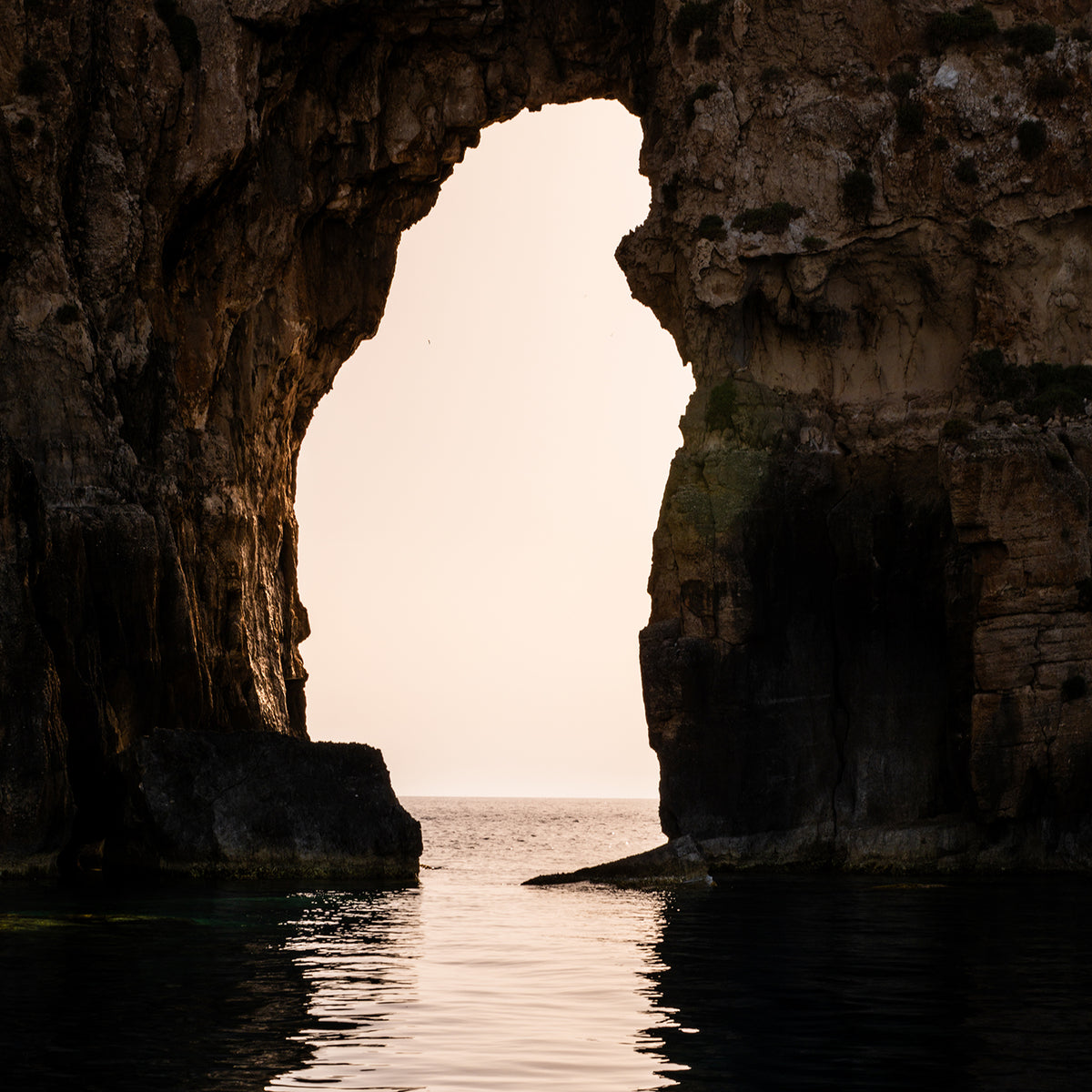 Warm sunlight passing through a natural sea arch above calm water near Pylos, Messinia, Greece.

