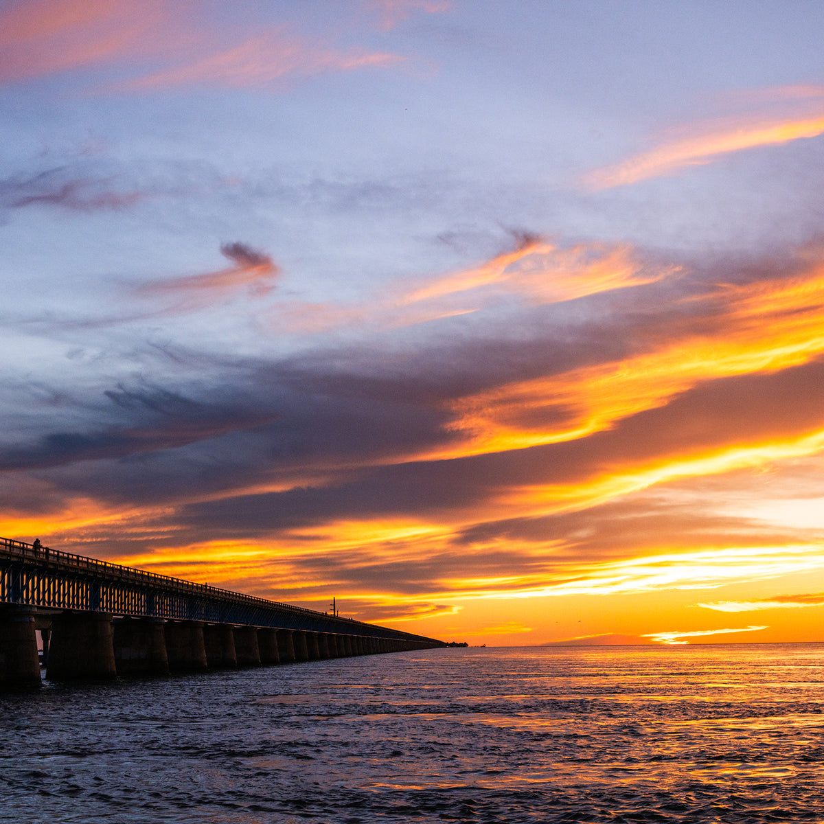 Seven Mile Bridge at dusk beneath a dramatic orange and blue sunset sky over the water in the Florida Keys.
