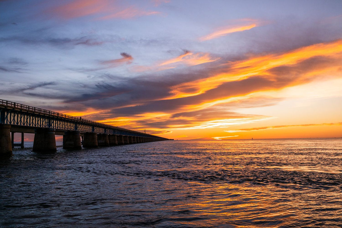 Seven Mile Bridge stretching across the water in the Florida Keys beneath orange and indigo clouds at dusk.